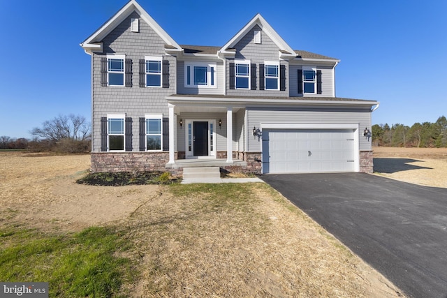 view of front of house featuring stone siding, covered porch, driveway, and an attached garage