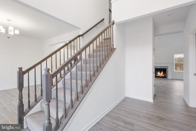 stairs with a lit fireplace, an inviting chandelier, baseboards, and wood finished floors