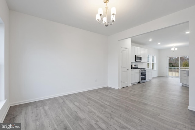 unfurnished living room with recessed lighting, light wood-type flooring, baseboards, and an inviting chandelier