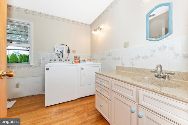 laundry area with cabinets, light hardwood / wood-style flooring, sink, tile walls, and washing machine and dryer