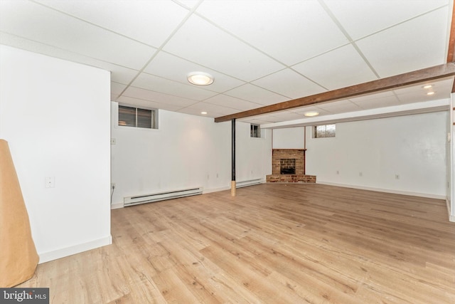 basement featuring a drop ceiling, a brick fireplace, light hardwood / wood-style flooring, and baseboard heating