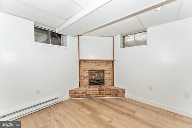 unfurnished living room featuring a paneled ceiling, a brick fireplace, light hardwood / wood-style floors, and baseboard heating