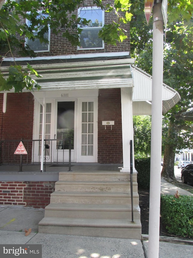 view of exterior entry with covered porch and brick siding