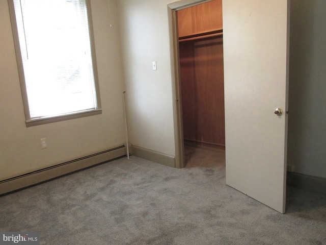 unfurnished bedroom with a closet, light colored carpet, a walk in closet, and baseboard heating