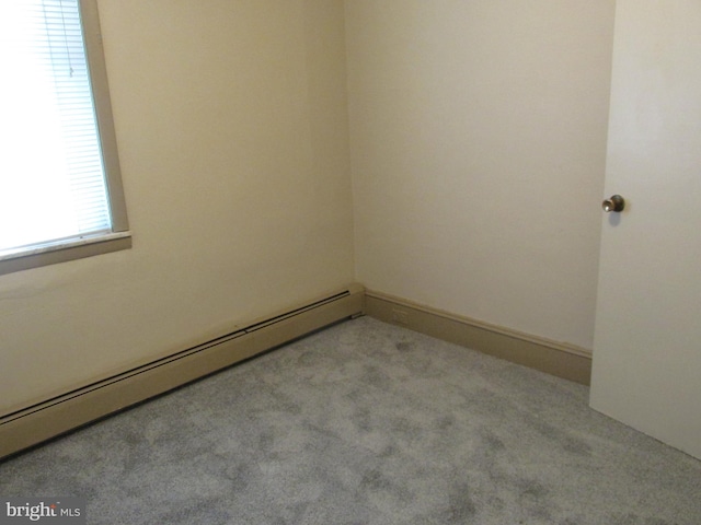 spare room featuring a baseboard heating unit and light carpet