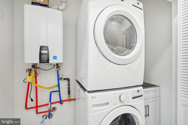 clothes washing area featuring stacked washer / dryer, tankless water heater, and cabinets