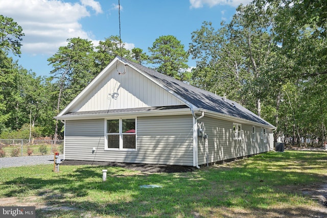 view of side of property featuring roof with shingles, a lawn, and fence