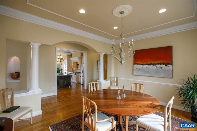 dining room with dark wood-type flooring, a notable chandelier, decorative columns, and ornamental molding