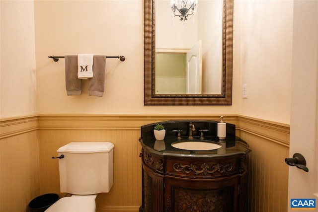 half bath with wainscoting, vanity, and toilet