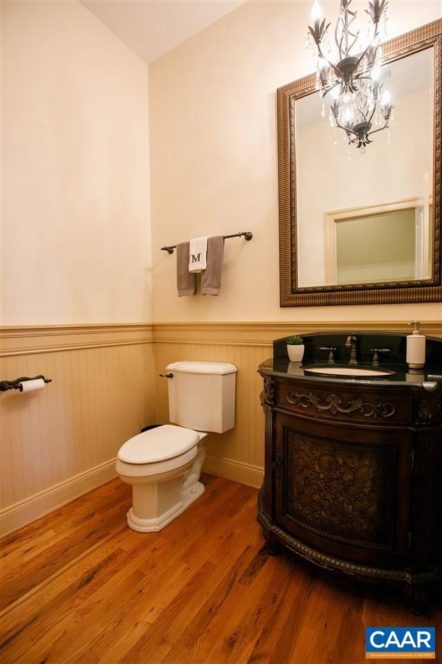 bathroom with toilet, a wainscoted wall, wood finished floors, vanity, and an inviting chandelier