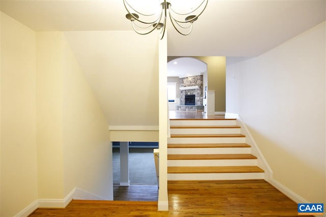 stairs with a notable chandelier, a fireplace, baseboards, and wood finished floors