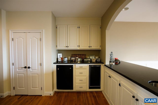 kitchen with arched walkways, white cabinets, dark countertops, dark wood-type flooring, and refrigerator