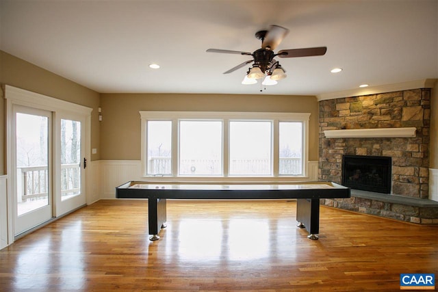 recreation room with a wainscoted wall, a stone fireplace, wood finished floors, and recessed lighting