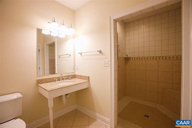 full bath featuring tile patterned flooring, toilet, a sink, baseboards, and a tile shower