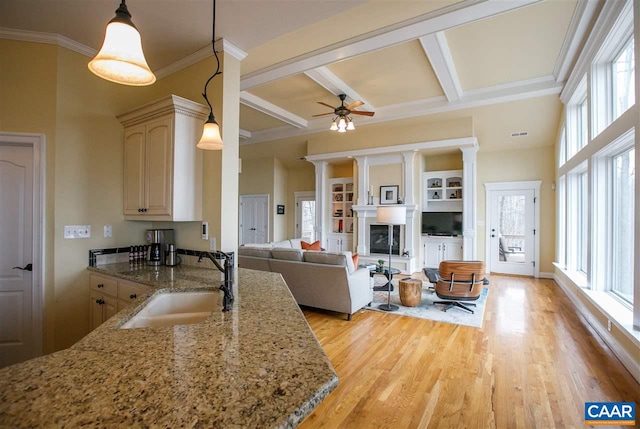 kitchen featuring a fireplace with raised hearth, hanging light fixtures, light wood-style floors, a sink, and beamed ceiling