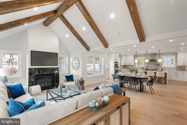 living room with beam ceiling, light hardwood / wood-style floors, high vaulted ceiling, and a premium fireplace