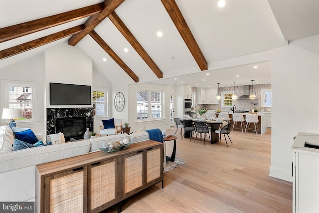 living room with beam ceiling, a fireplace, high vaulted ceiling, and light hardwood / wood-style flooring