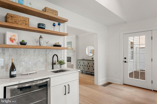 kitchen featuring light stone countertops, light wood-type flooring, beverage cooler, sink, and white cabinetry