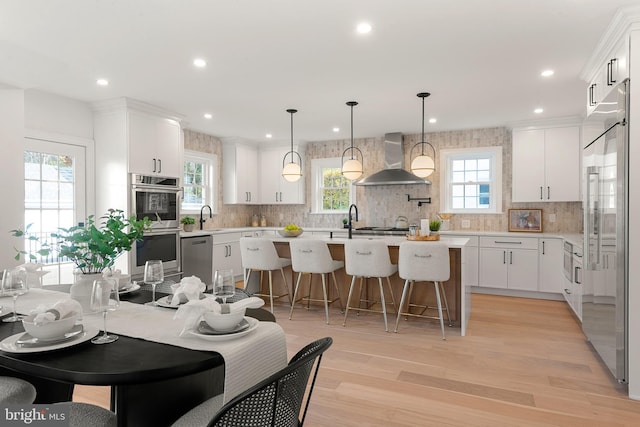 kitchen featuring white cabinetry, sink, wall chimney range hood, pendant lighting, and a kitchen island