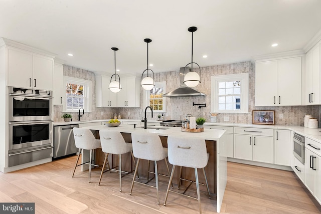 kitchen featuring white cabinets, wall chimney exhaust hood, a kitchen island, and stainless steel appliances