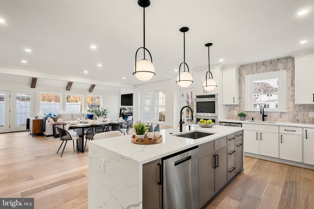 kitchen featuring a center island with sink, white cabinets, hanging light fixtures, appliances with stainless steel finishes, and beam ceiling