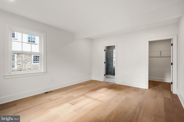 unfurnished bedroom with connected bathroom, a spacious closet, a closet, and light wood-type flooring