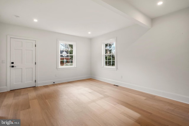 spare room featuring beamed ceiling and light hardwood / wood-style flooring