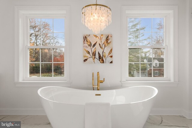 bathroom featuring a healthy amount of sunlight, a bath, and an inviting chandelier