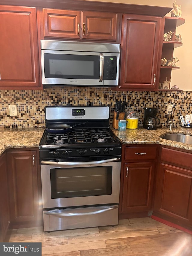 kitchen with light stone countertops, light hardwood / wood-style flooring, appliances with stainless steel finishes, sink, and decorative backsplash