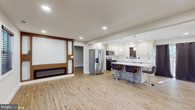 kitchen with a breakfast bar, stainless steel appliances, white cabinets, light hardwood / wood-style floors, and a kitchen island