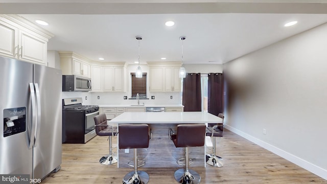 kitchen featuring appliances with stainless steel finishes, light wood-type flooring, a breakfast bar, a kitchen island, and hanging light fixtures