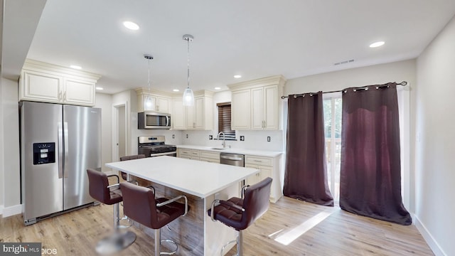 kitchen featuring a kitchen breakfast bar, sink, light wood-type flooring, decorative light fixtures, and stainless steel appliances