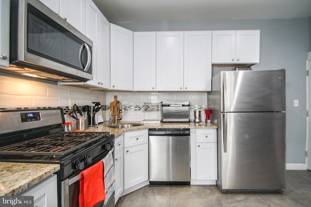 kitchen with white cabinets, sink, backsplash, appliances with stainless steel finishes, and light stone countertops