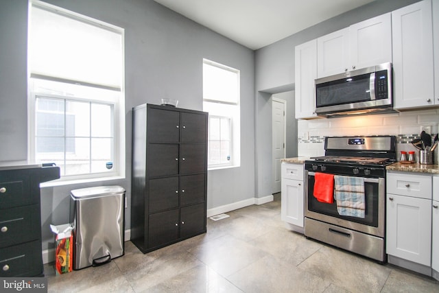 kitchen featuring a wealth of natural light, stainless steel appliances, stone countertops, and white cabinetry