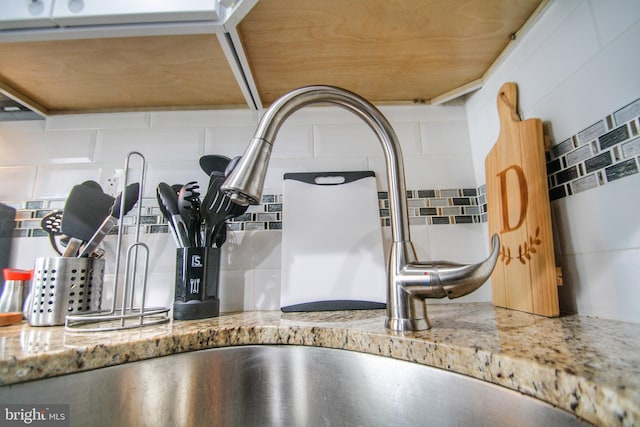 details featuring light stone countertops, tasteful backsplash, and sink