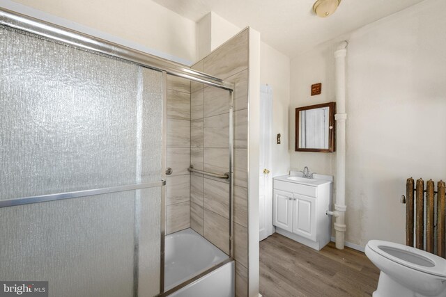 full bathroom featuring enclosed tub / shower combo, vanity, radiator heating unit, hardwood / wood-style flooring, and toilet