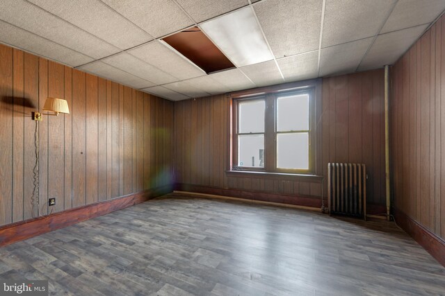 spare room featuring radiator, wooden walls, dark hardwood / wood-style floors, and a paneled ceiling