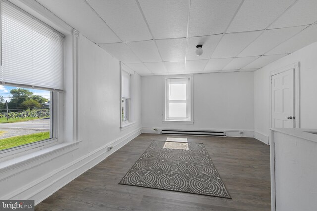 interior space featuring a drop ceiling, a baseboard heating unit, and dark hardwood / wood-style flooring