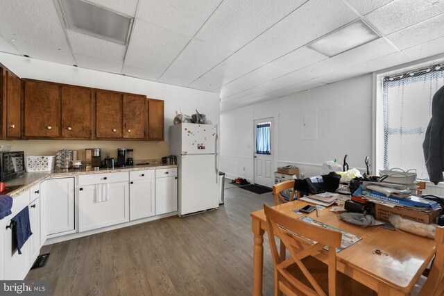 kitchen with wood-type flooring, white refrigerator, a drop ceiling, and white cabinetry