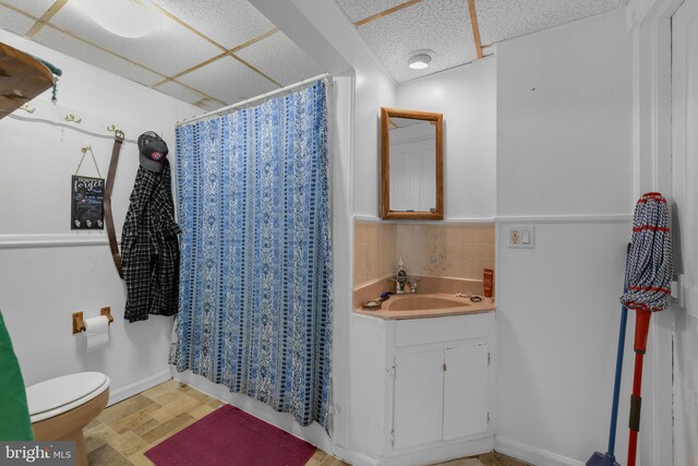 bathroom featuring a drop ceiling, vanity, toilet, and a shower with curtain