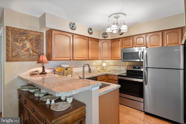 kitchen with an inviting chandelier, appliances with stainless steel finishes, hanging light fixtures, kitchen peninsula, and a breakfast bar