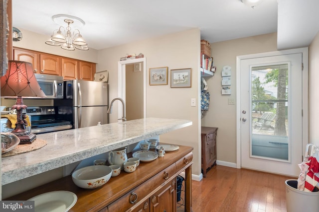 kitchen featuring an inviting chandelier, light wood-type flooring, decorative light fixtures, appliances with stainless steel finishes, and sink