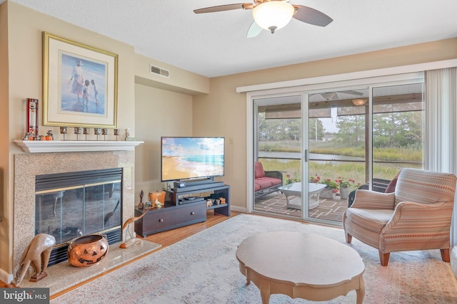 living area with visible vents, plenty of natural light, a tiled fireplace, and wood finished floors