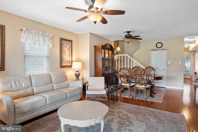 living area featuring baseboards, a ceiling fan, hardwood / wood-style floors, stairs, and a textured ceiling