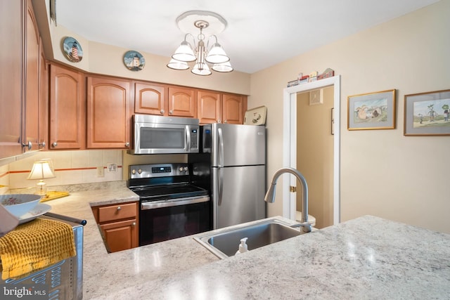 kitchen with stainless steel appliances, brown cabinets, a sink, and an inviting chandelier