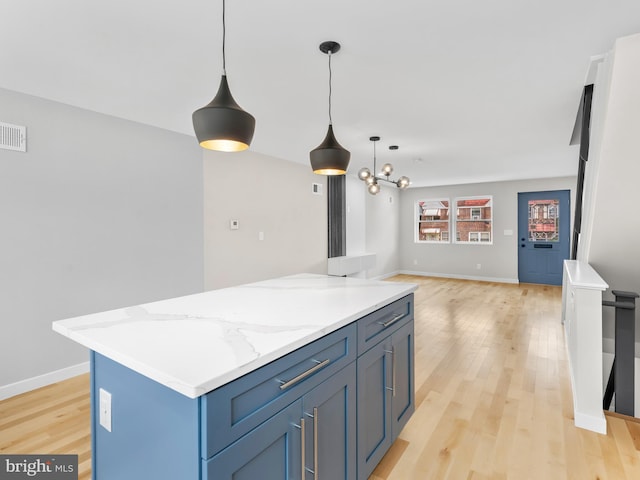 kitchen with hanging light fixtures, light stone counters, a center island, and light hardwood / wood-style floors