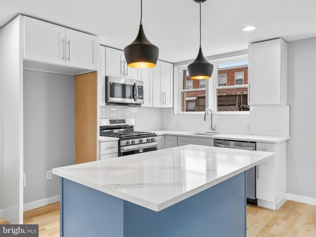 kitchen with pendant lighting, white cabinetry, backsplash, sink, and appliances with stainless steel finishes