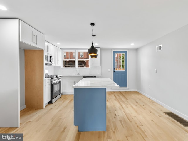 kitchen with pendant lighting, a kitchen island, stainless steel appliances, and white cabinets