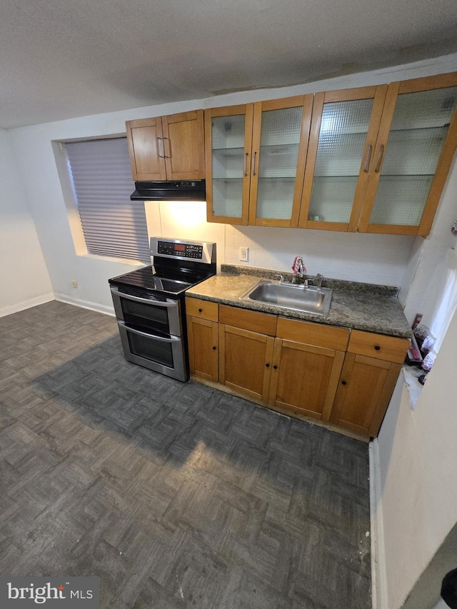 kitchen with double oven range, a sink, glass insert cabinets, under cabinet range hood, and brown cabinets