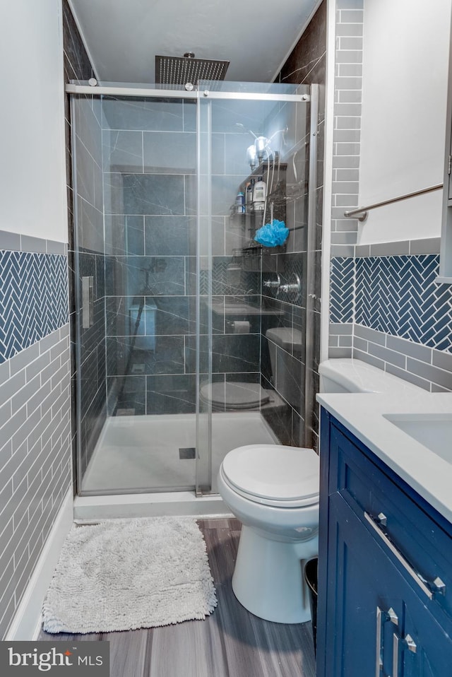 bathroom featuring tile walls, hardwood / wood-style floors, a shower with shower door, vanity, and toilet